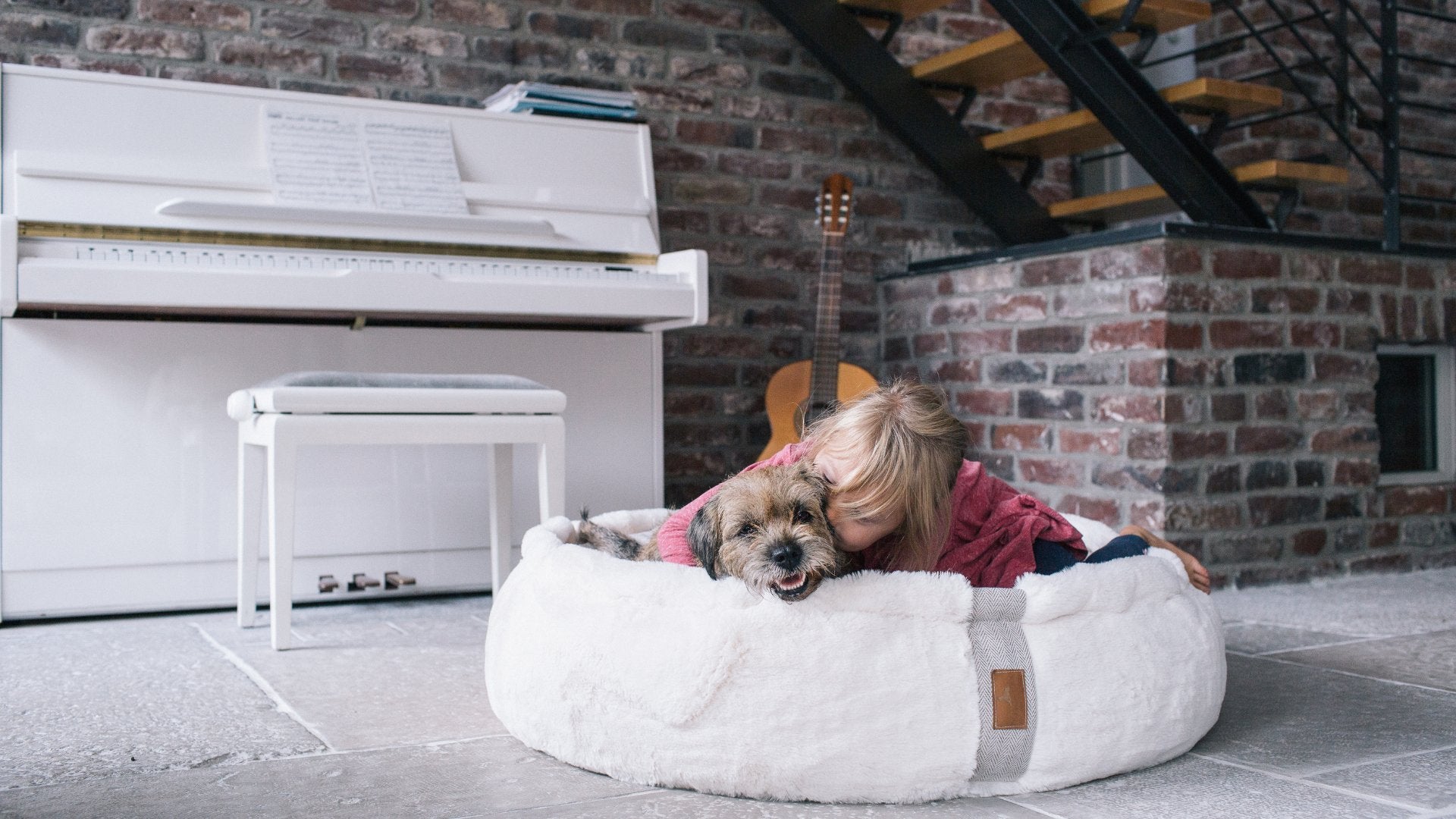 Kleines Mädchen kuschelt liebevoll mit wuscheligem Hund im weißen flauschigen orthopädischen Hundebett Hyggebed Original im Wohnzimmer