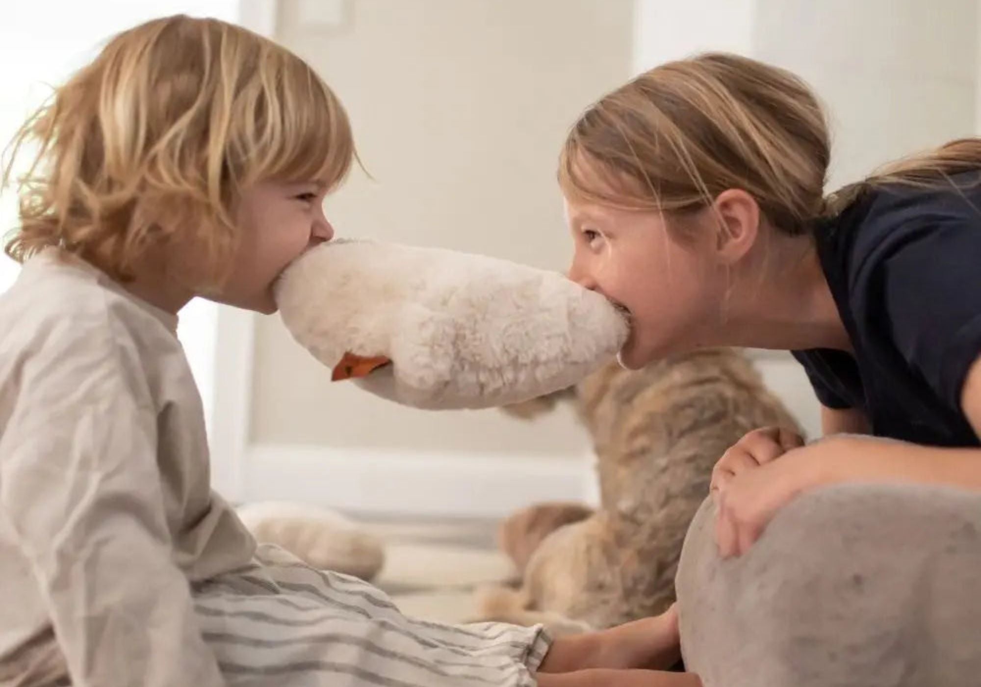 Zwei Kinder spielen im Wohnzimmer gemeinsam mit einem flauschigen Hyggebed Kuschelkissen