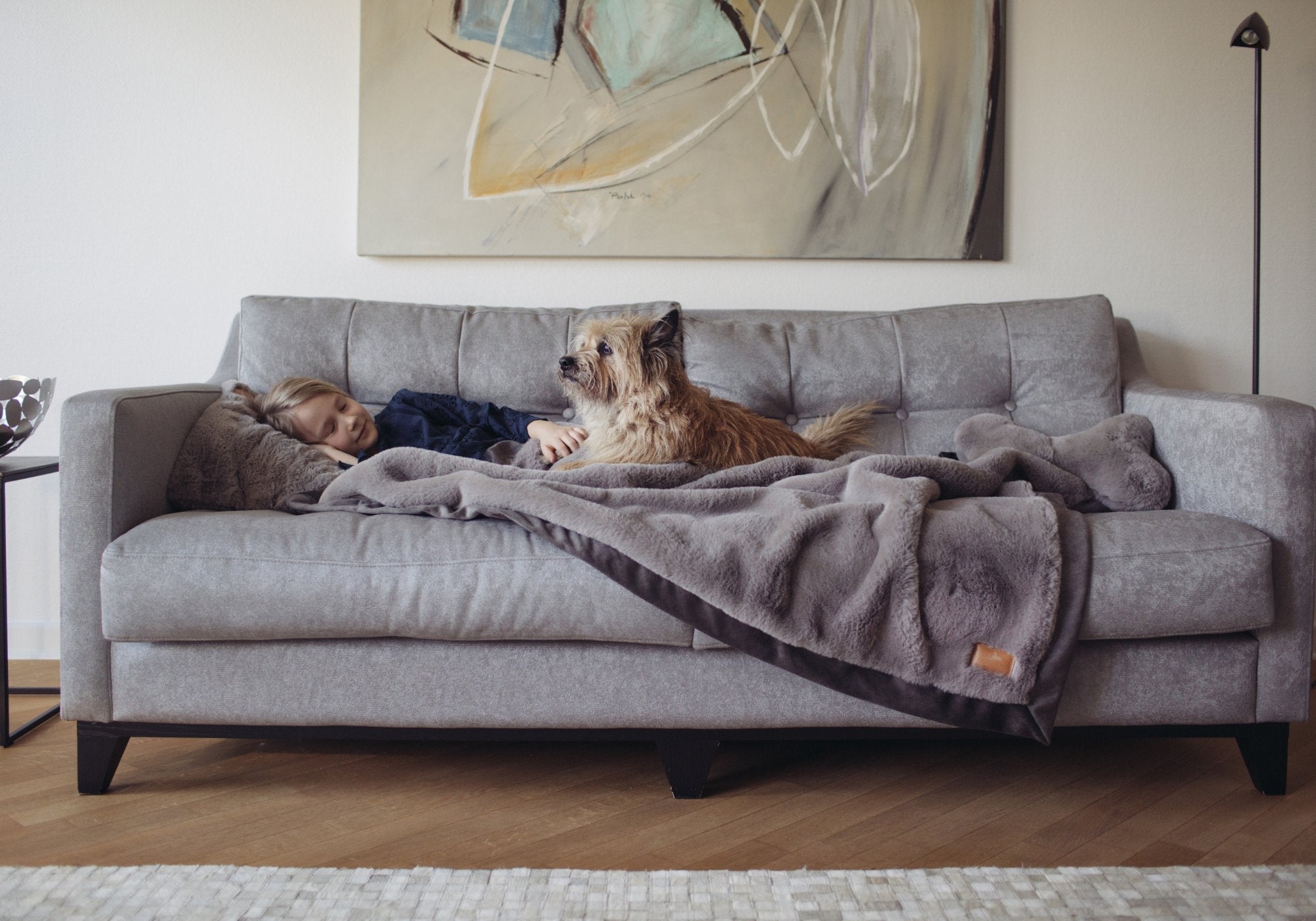 Mädchen kuschelt mit Hund auf einem grauen Sofa unter einer luxuriösen grauen Hyggebed Kuscheldecke