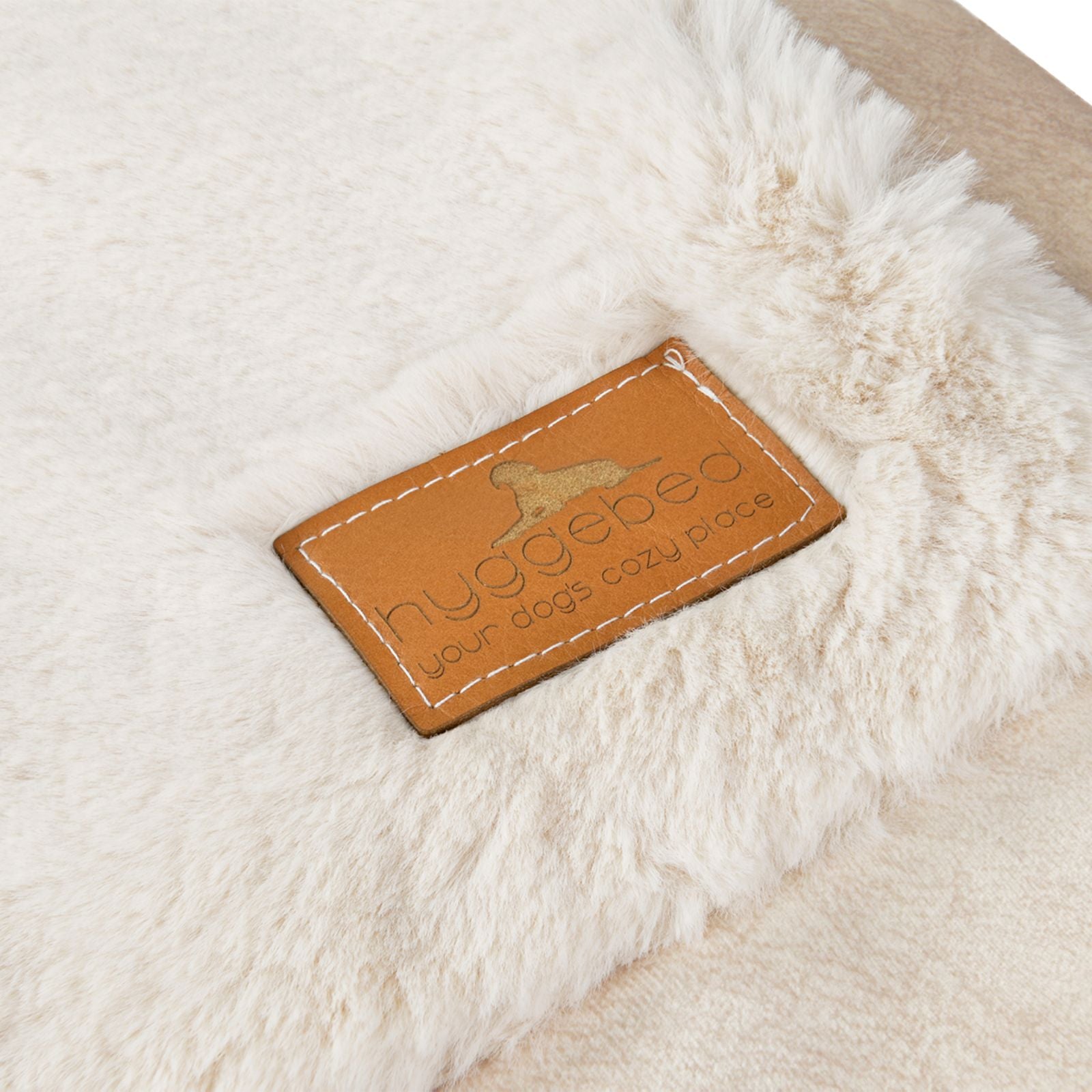Nahaufnahme des edlen braunen Leder-Labels mit eingeprägtem Hyggebed Logo auf dem cremeweißen Ivory Plüsch-Stoff