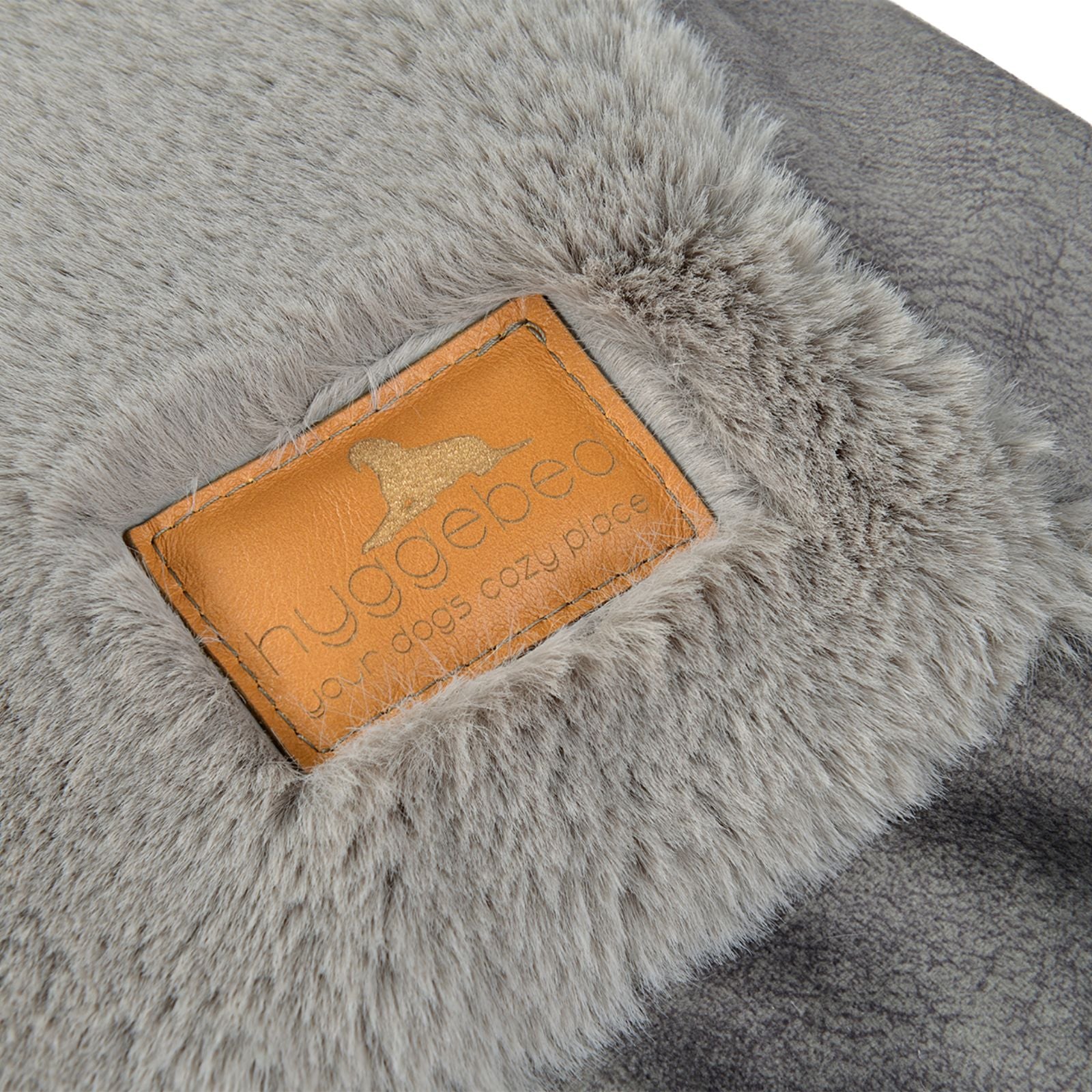 Nahaufnahme des edlen braunen Leder-Labels mit eingeprägtem Hyggebed Logo auf dem grauen Webpelz-Stoff