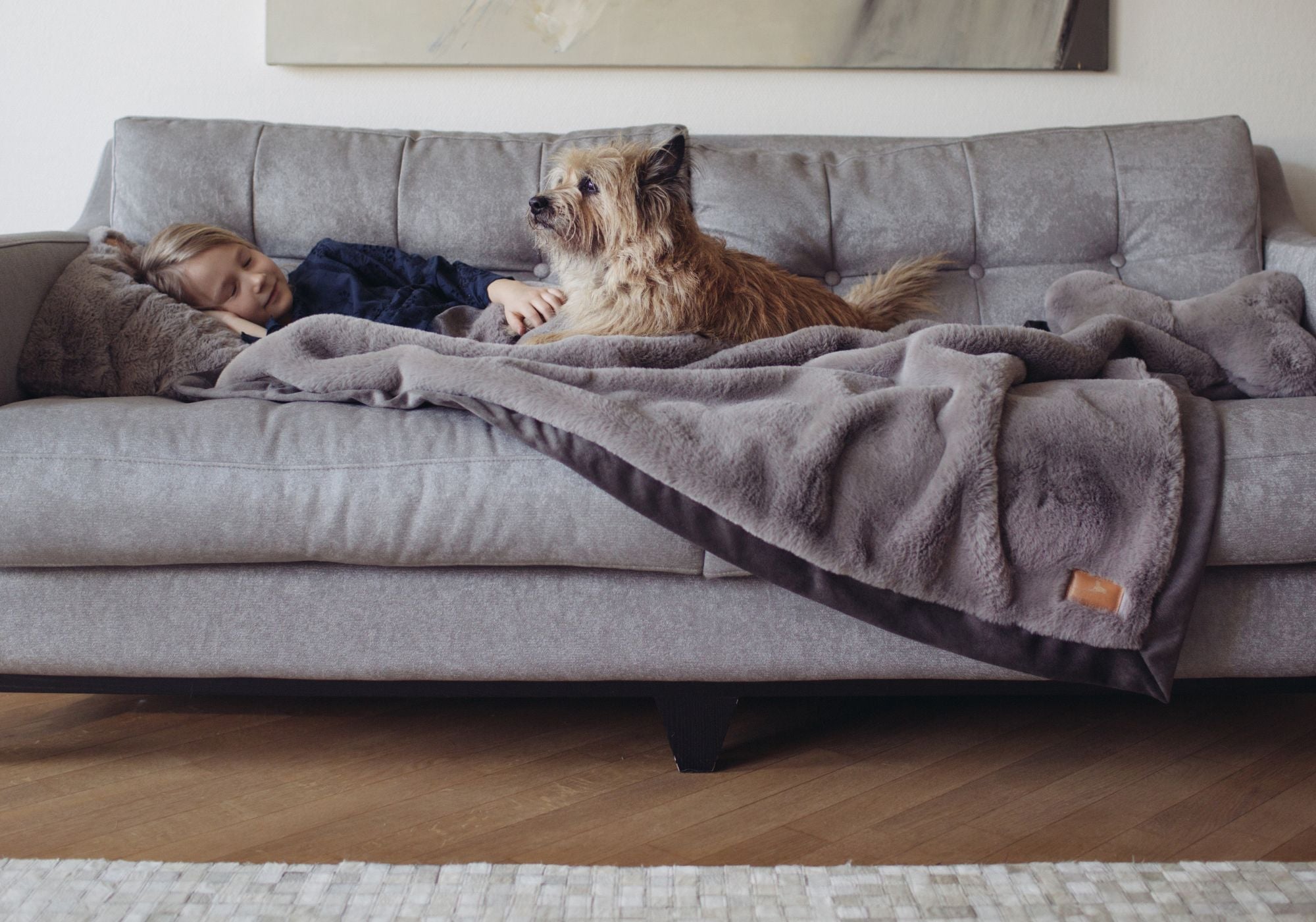 Mädchen kuschelt mit seinem Hund auf dem Sofa unter einer großen grauen Hyggeblanket Kuscheldecke