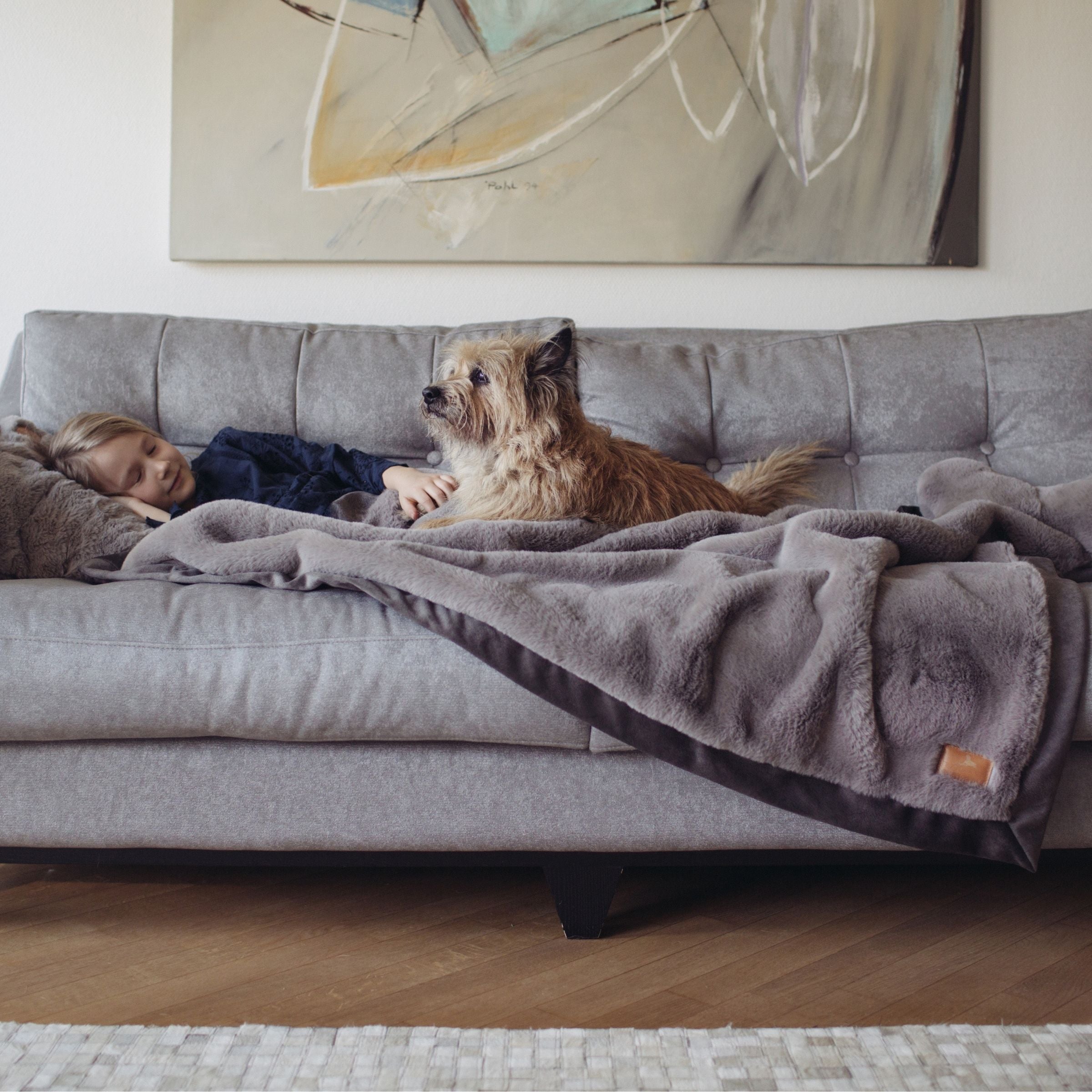 Mädchen liegt mit Terrier Hund gemütlich auf grauem Sofa unter der grauen Hyggeblanket Kuscheldecke
