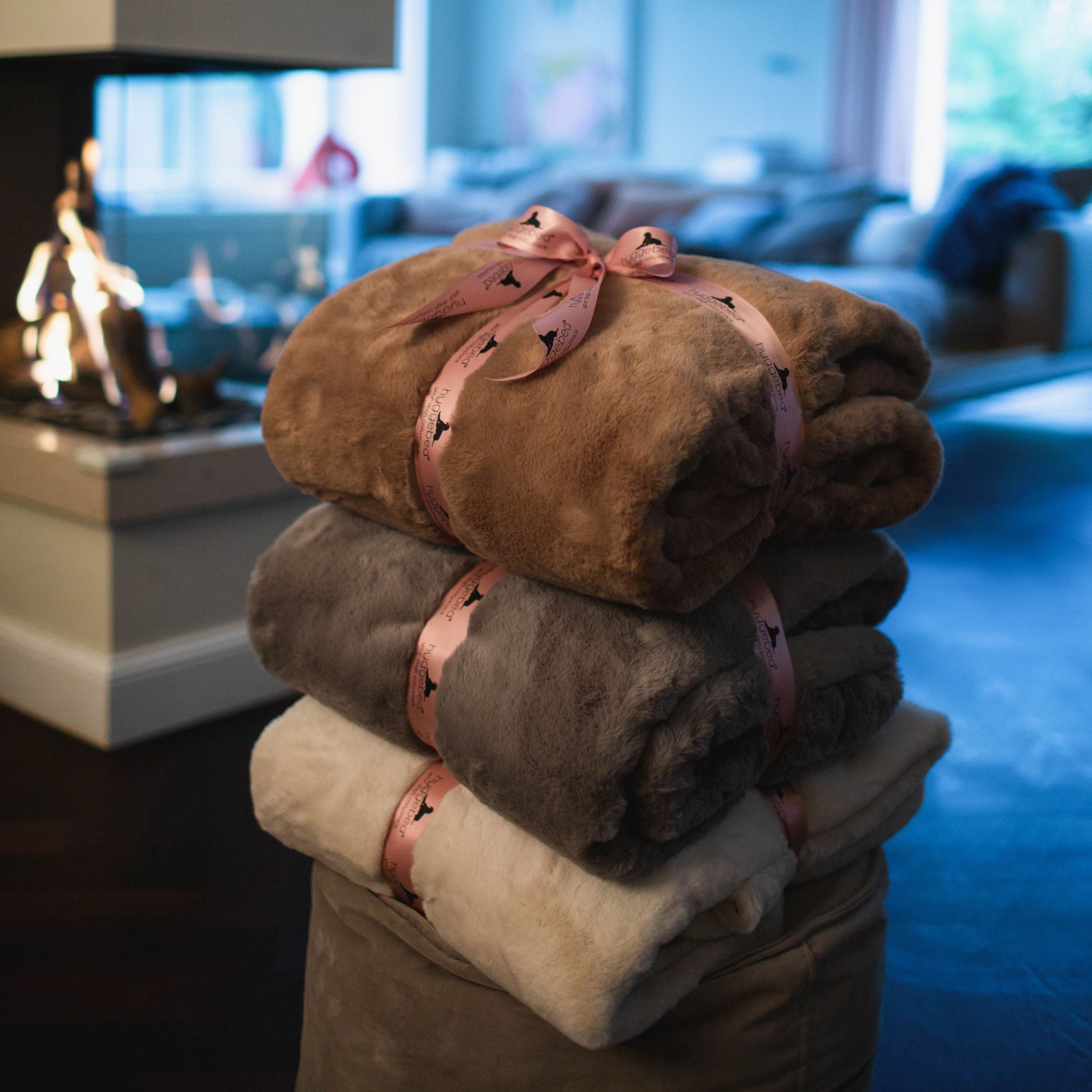 Ein Stapel aus drei verpackten Hyggeblanket Kuscheldecken für Menschen in den Farben Maroon, Stone und Ivory